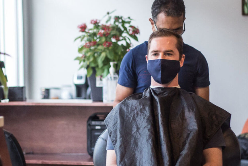 A barber giving a haircut to a man wearing a mask