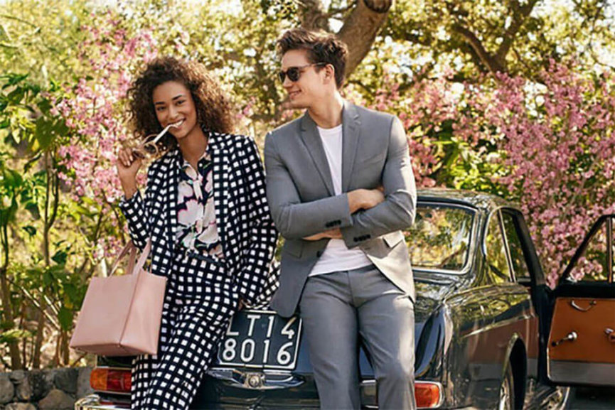 A woman and a man dressed fashionably leaning against a car.