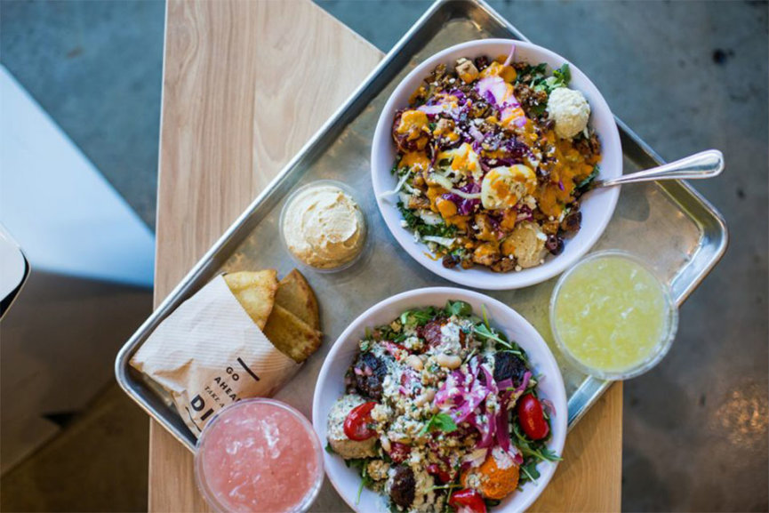 Two bowls of food on a metal tray, sitting next to two colorful drinks.