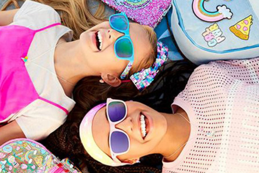 Two girls smiling while looking up at the sky wearing colorful sunglasses