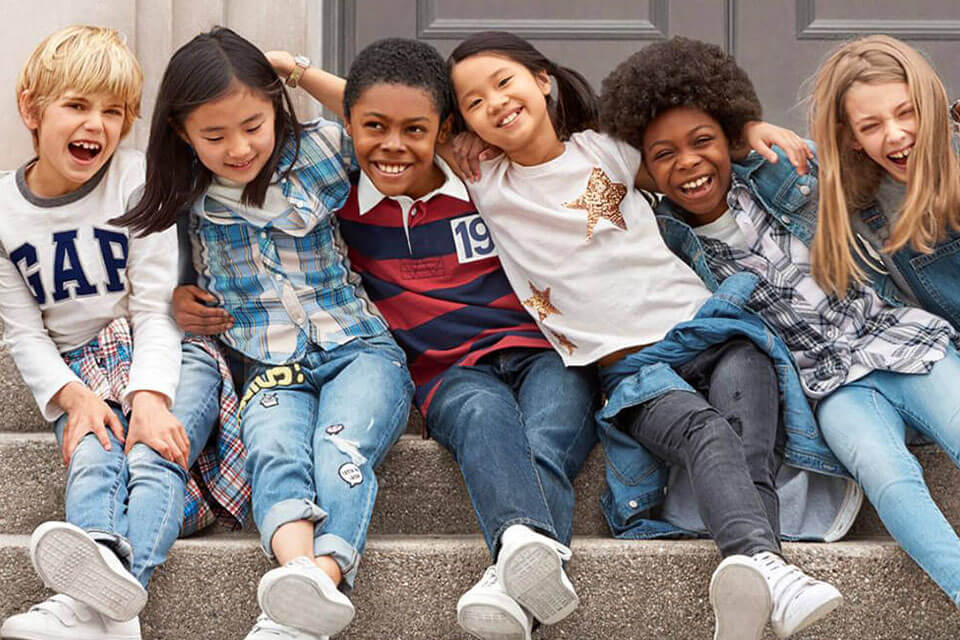 Six kids sitting on a step with their arms around each other waring Gap clothing