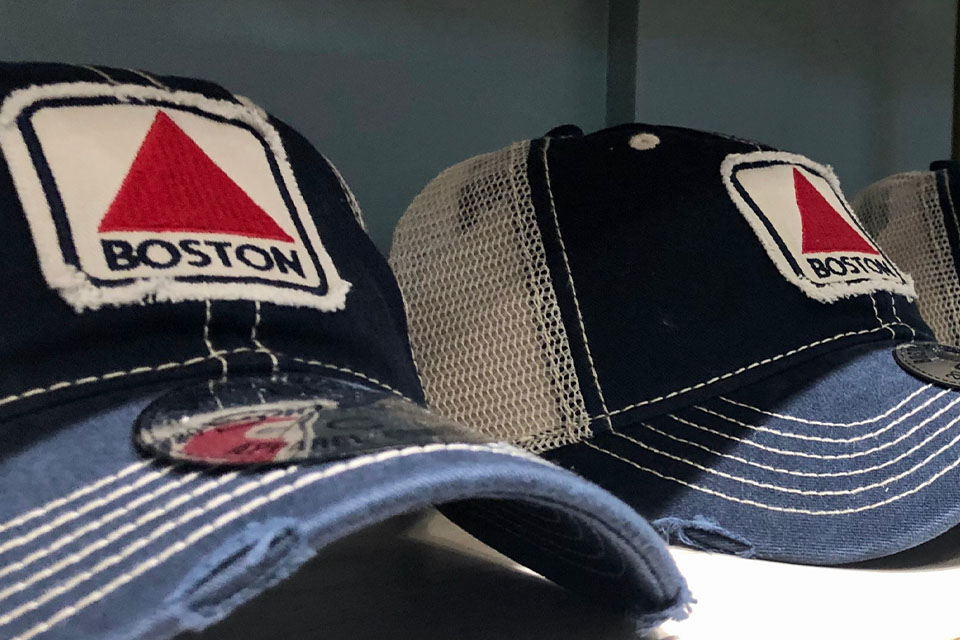 Two baseball caps sitting on a shelf with the word Boston on them