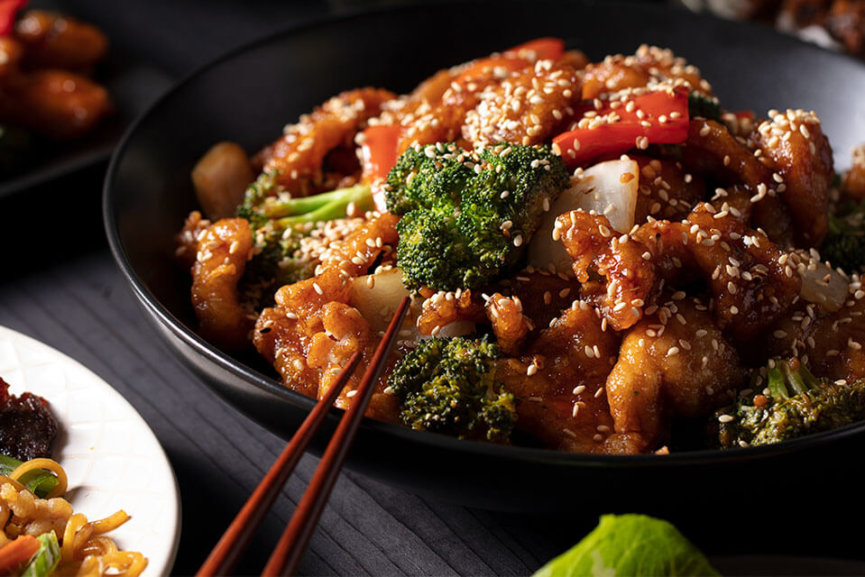 A bowl of sesame chicken, peppers, broccoli, and rice