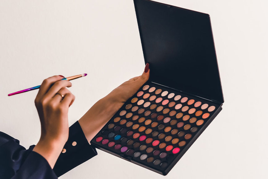 A woman holding a makeup pallete and a make up brush